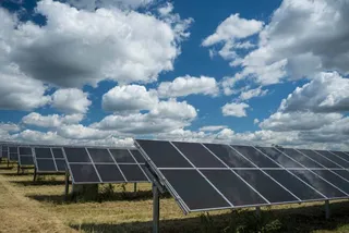 Rânduri de panouri solare sunt instalate pe un câmp sub un cer albastru cu nori albi plutitori.