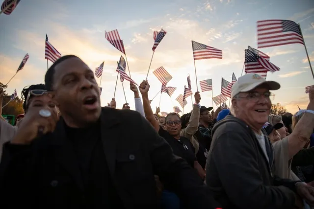 Oamenii ridică diverse steaguri americane sub un cer luminos la apusul soarelui.