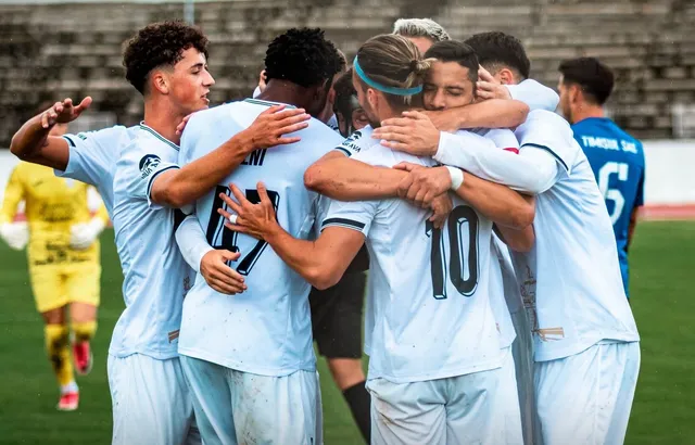 Un grup de jucători de fotbal în echipamente albastre se îmbrățișează pe un teren de sport.