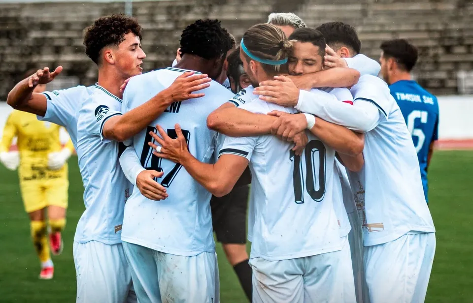 Un grup de jucători de fotbal în echipamente albastre se îmbrățișează pe un teren de sport.