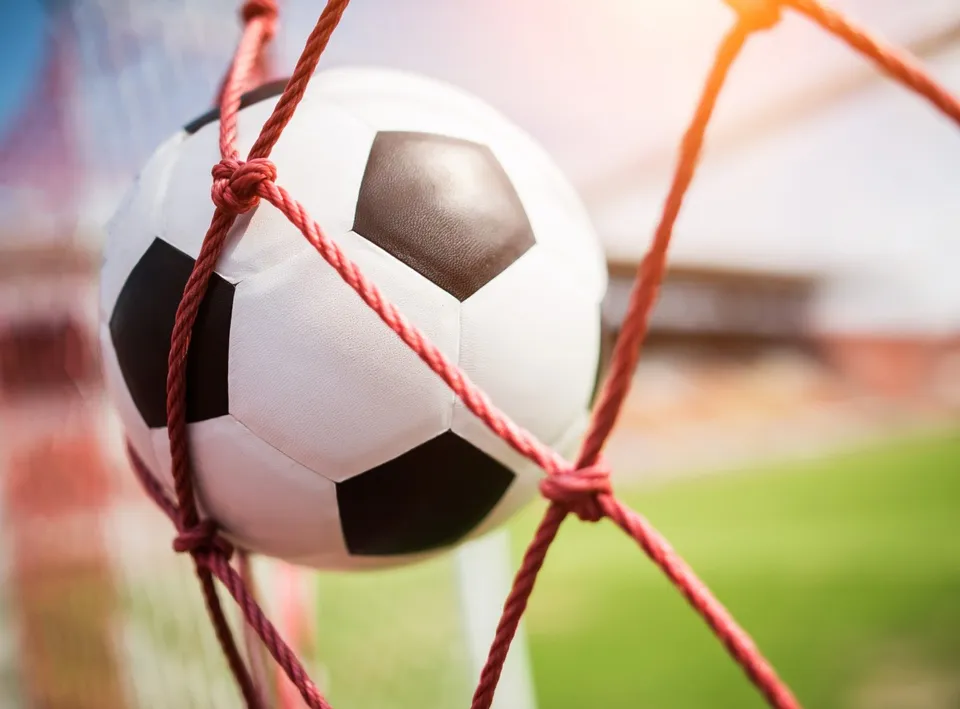 Un fotbal alb cu pete negre este capturat în plasa unei porți de fotbal pe un teren de sport.