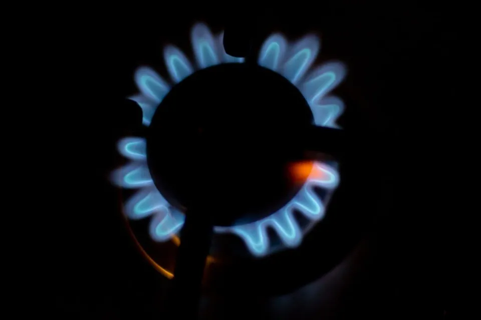 O flacără albastră de gaz arde într-un arzător de aragaz pe un fundal întunecat.