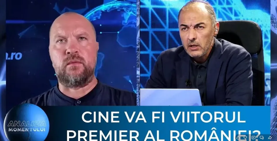 Un bărbat cu barbă poartă un tricou negru, iar celălalt poartă un sacou închis peste o cămașă, fiind așezați în fața unui fundal albastru.