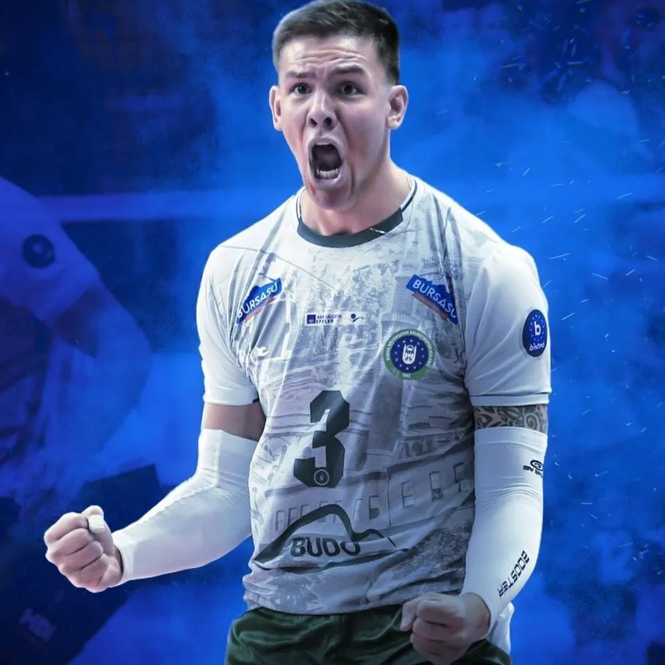 Un bărbat cu tricou alb și mâneci lungi albe stă cu pumnii strânși și gura deschisă într-o sală de sport.