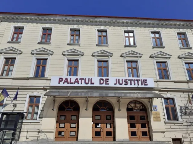 O clădire cu mai multe etaje prezintă ferestre dreptunghiulare și un pridvor deasupra a trei uși de lemn cu panouri de sticlă.