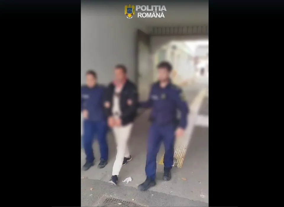 Trei bărbați în uniformă și unul în haine civile stau într-un spațiu acoperit, unul civil fiind în mijlocul grupului.