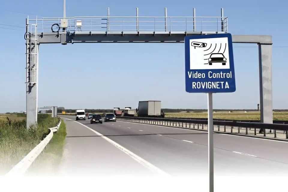 O structură metalică de tip portal traversează o autostradă pe unde circulă câteva vehicule sub un cer senin.