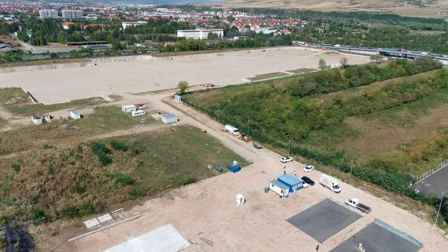 O vedere aeriană prezintă un teren mare și plat, cu câteva containere albe, vehicule și vegetație înconjurătoare sub un cer deschis.
