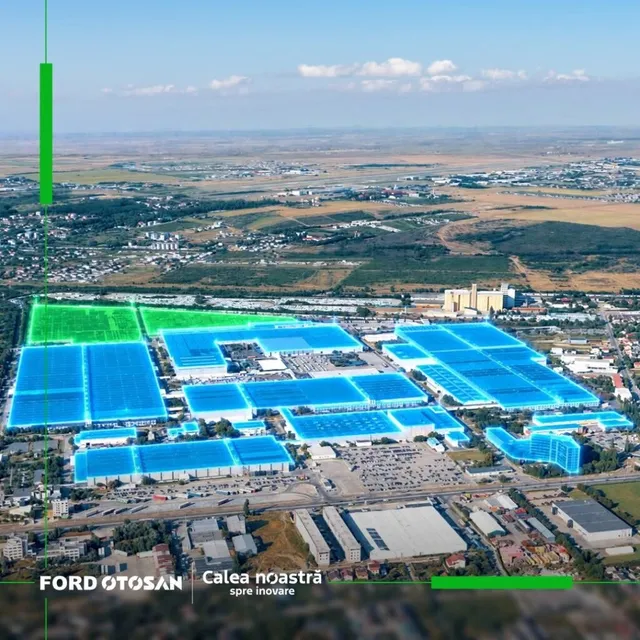 O vedere aeriană a unui complex industrial cu mai multe clădiri mari acoperite de panouri de culoare albastră sub un cer senin.