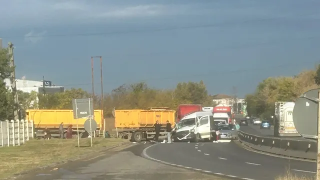 Două vehicule de marfă galbene și un camion alb sunt parcate pe marginea unui drum asfaltat lângă un gard de beton și vegetație.