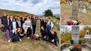 Un grup de elevi stă lângă două morminte înconjurate de flori într-un cimitir aflat pe un teren înclinat sub un cer înnorat.