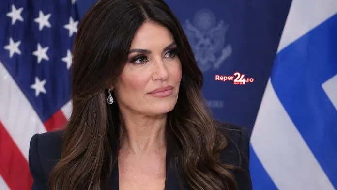 O femeie cu părul lung și brunet stă în fața unui steag american și al unui steag albastru cu dungi albe.