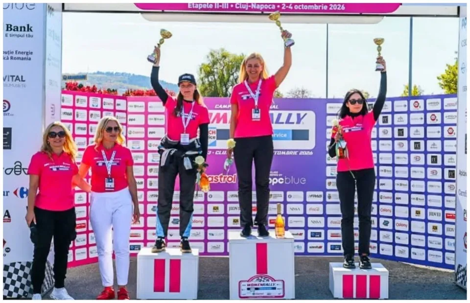 Patru femei în tricouri roz stau pe podiumuri albe, purtând trofee și medalii, în fața unui panou cu diverse logouri.