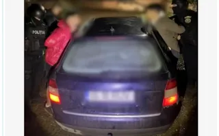 O mașină de culoare închisă este înconjurată de mai mulți oameni, dintre care unii poartă uniformă neagră cu inscripția POLITIA.