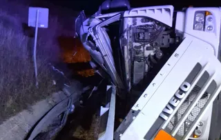 Un camion alb de marca Iveco este răsturnat pe o laterală, într-un mediu întunecat cu vegetație în fundal.