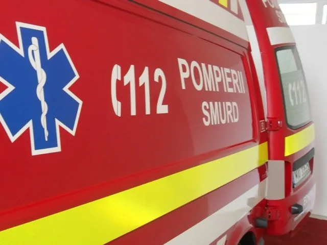 Un vehicul de serviciu roșu prezintă simbolul stelii vieții albastre și inscripții albe cu numărul 112, POMPIERII și SMURD.