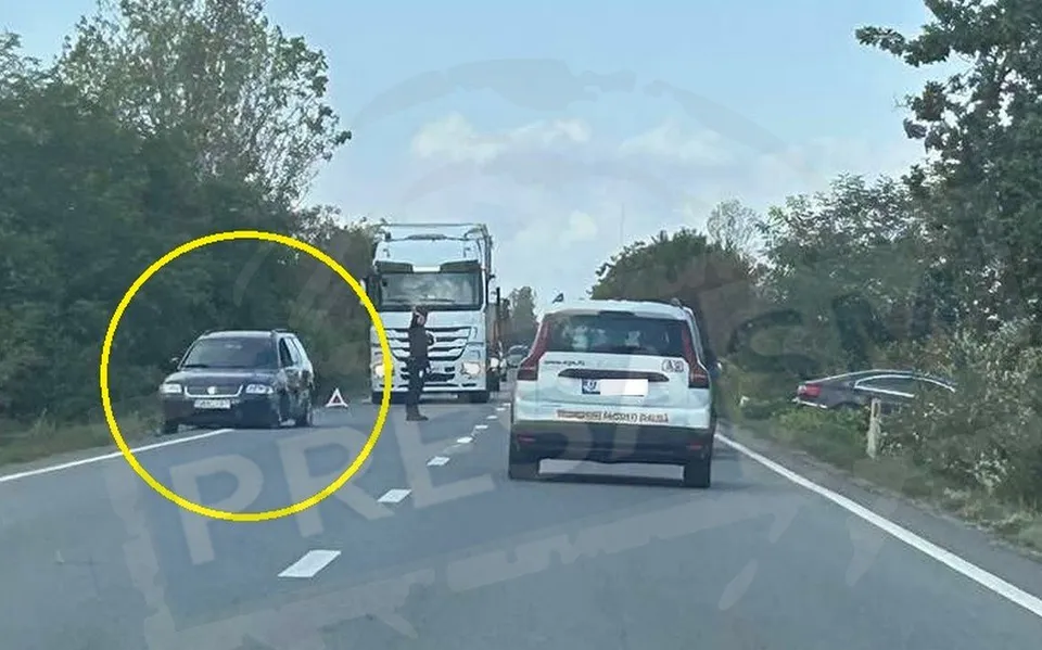 Un camion alb și un autoturism negru sunt poziționate pe o drum asfaltat lângă un vehicul alb și un alt autoturism gri.