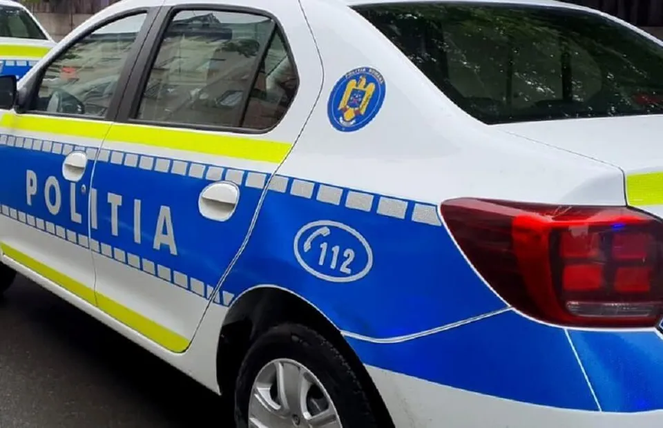 Partea laterală și spatele unei mașini de poliție albe cu marcaje albastre și galbene, afișând textul POLIȚIA și numărul de urgență 112.