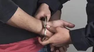 Mâinile unei persoane sunt prinse în cătușe de o altă persoană care poartă o cămașă închisă la culoare.