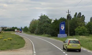 O drumuită asfaltată curbează spre stânga, cu o mașină galbenă în prim plan și un panou albastru de bun venit la Ghimbav în fundal.