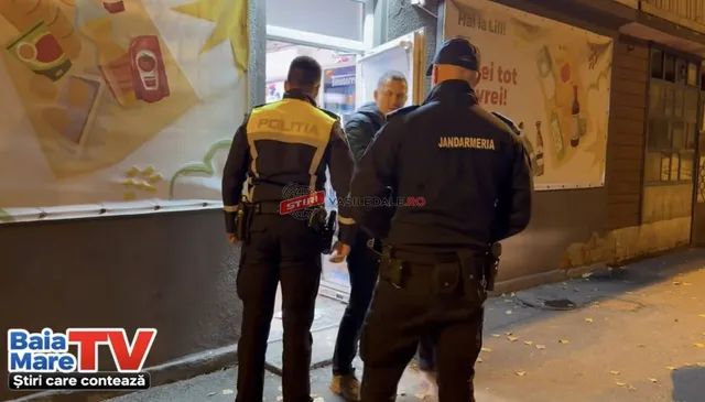 Doi polițiști în uniformă stau în fața unui magazin, observând un bărbat în picioare lângă intrare.