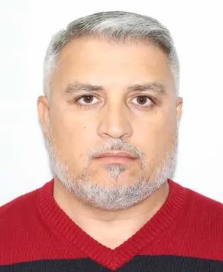 Un bărbat cu părul și barba gri poartă un pulover roșu cu guler în formă de V.