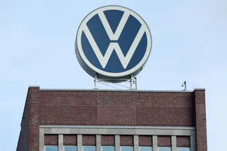 Un semn circular cu literele VW este montat pe partea superioară a unei clădiri din cărămidă sub un cer senin.
