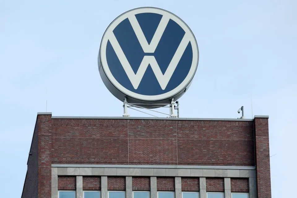 Un semn circular cu literele VW este montat pe partea superioară a unei clădiri din cărămidă sub un cer senin.
