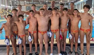 Un grup de adolescenți fără tricou, purtând costume de baie colorate, stă în rând într-o piscină cu un adult în spate.