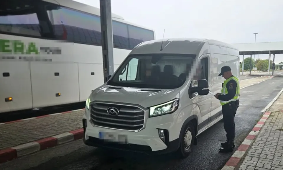 Un vehicul utilitar alb este oprit pe o stradă lângă un autobuz alb, în timp ce un agent în uniformă stă lângă portiera șoferului.