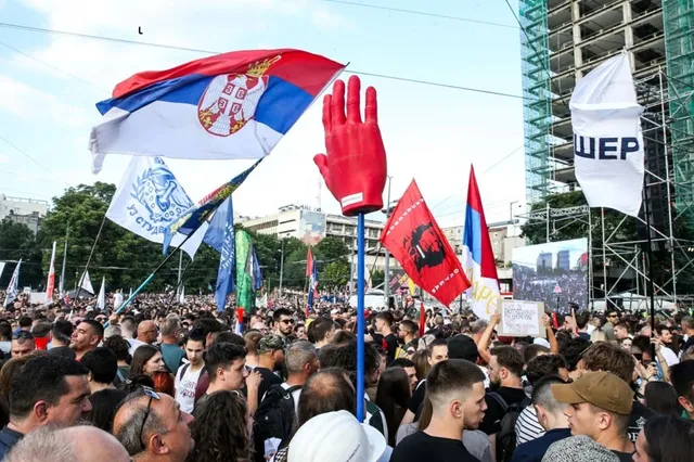 O mulțime de oameni adună steaguri colorate și un stâlp cu o mănușă roșie sub un cer luminos.