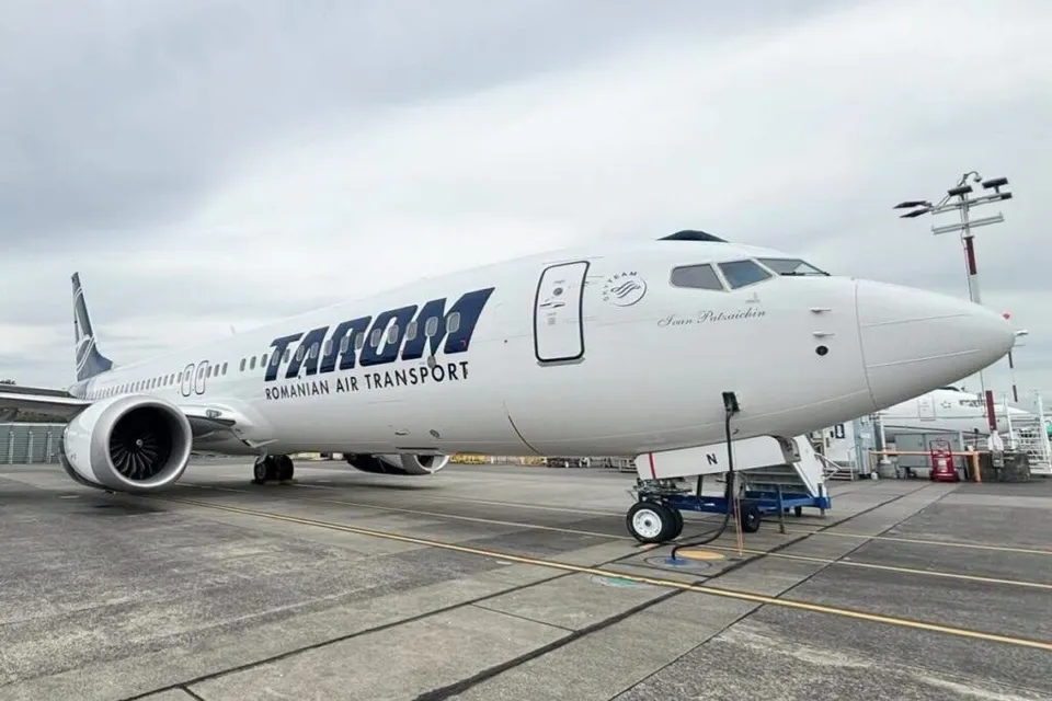 Un avion alb cu inscripția TAROM Romanian Air Transport este parcat pe o pistă de aeroport sub un cer înnorat.