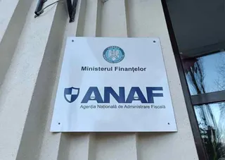 Un panou alb cu siglul Ministerului Finanțelor și textul ANAF este montat pe o fațadă de clădire cu strii verticale.