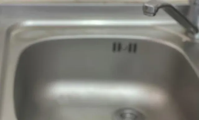 O chiuvetă metalică de bucătărie cu un robinet deasupra, prezentând câteva marcaje negre pe interiorul suprafeței de inox.
