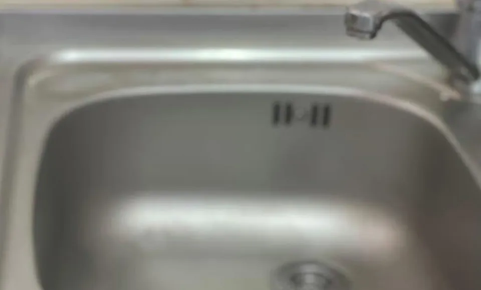 O chiuvetă metalică de bucătărie cu un robinet deasupra, prezentând câteva marcaje negre pe interiorul suprafeței de inox.