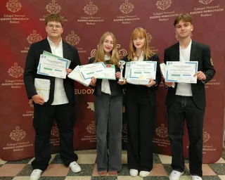 Patru persoane stau în picioare în fața unui fundal roșu, ținând diplome și un trofeu argintiu.