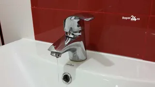 Un robinet cromat este montat pe o chiuvetă albă, lăsând un fir subțire de apă să curgă din mulutul acestuia.