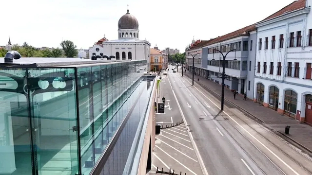 O stradă cu clădiri pe o parte și o structură de sticlă în prim-plan, cu un edifício cu cupolă în fundal.