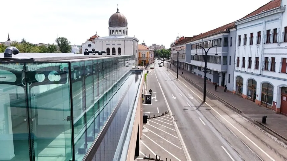 O stradă cu clădiri pe o parte și o structură de sticlă în prim-plan, cu un edifício cu cupolă în fundal.