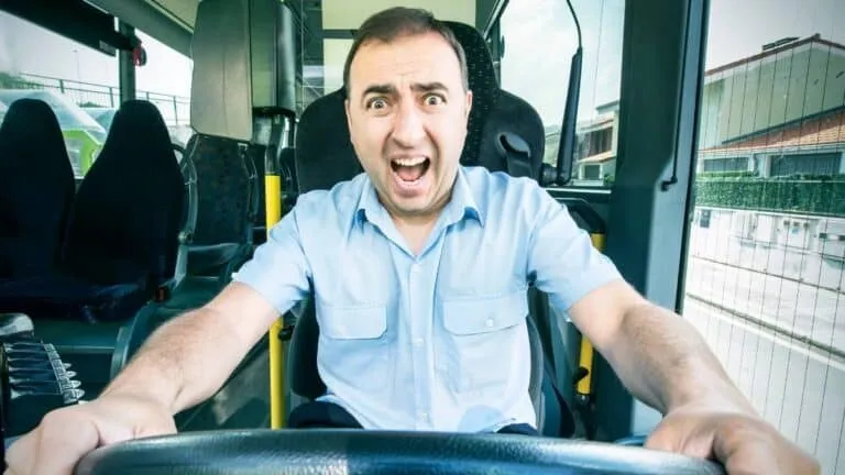 Un bărbat cu cămașă albastră stă la volanul unui vehiv, având gura deschisă și ochii măriți.