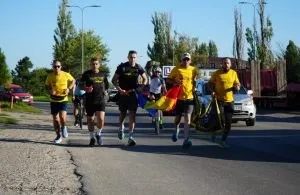 Cinci bărbați în haine sportive de culoare galbenă și neagră merg pe un drum asfaltat sub un cer senin.