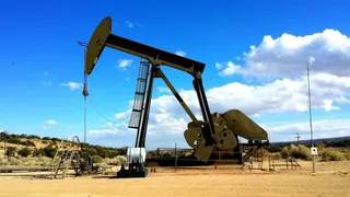 O unitate de pompare a petrolului este poziționată pe un teren arid sub un cer albastru cu nori albi.