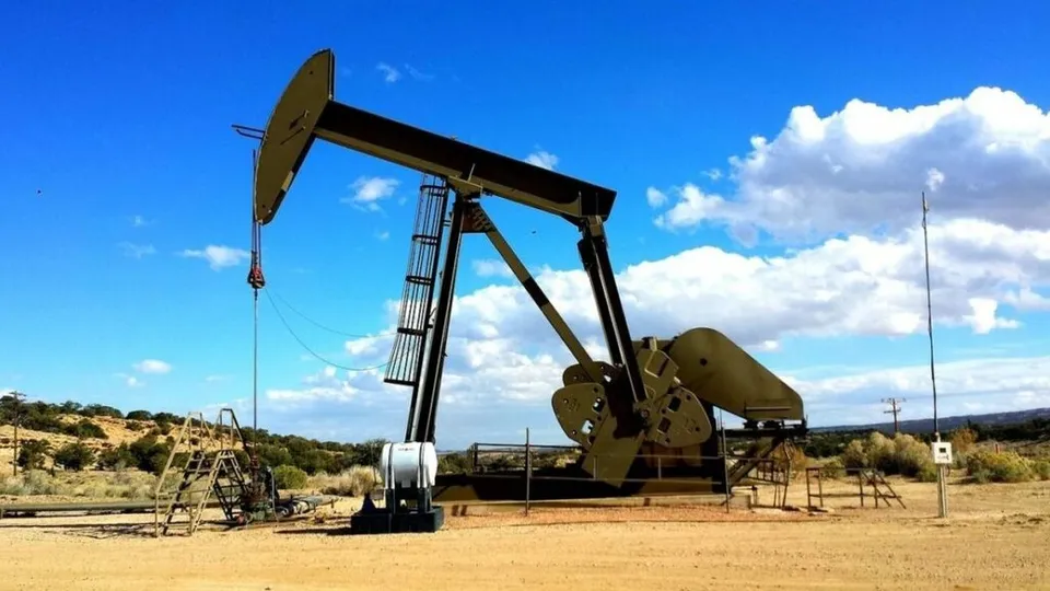 O unitate de pompare a petrolului este poziționată pe un teren arid sub un cer albastru cu nori albi.