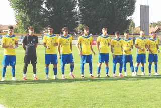 O echipă de fotbaliști stă în rând pe un teren de gazon verde, purtând echipamente sportive galbene și albastre sau negre.