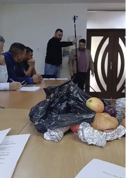 Un sac de plastic negru deschis conține fructe și produse de panificație pe o masă de lemn lângă câteva foi de hârtie albe.