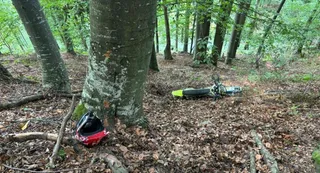 Un cască de motociclistă roșu și neagră este situată pe solul acoperit de frunze uscate lângă un copac într-o pădure.