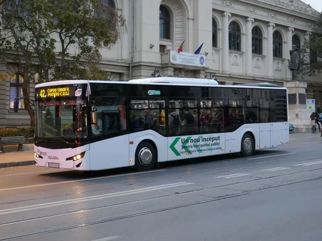 Un autobuz alb cu detalii verzi circulă pe un drum asfaltat în fața unei clădiri mari cu ferestre arcuite.