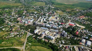 O vedere aeriană prezintă o zonă urbană cu clădiri diverse, drumuri și terenuri verzi înconjurate de câmpuri agricole.