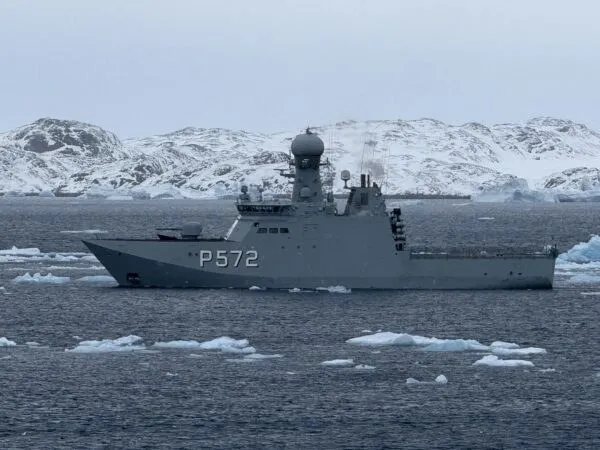 Un vas gri cu numărul P572 navighează pe apă într-un peisaj cu munți acoperiți de zăpadă și fragmente de gheață.