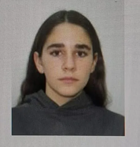 O adolescentă cu părul lung și întunecat poartă un hanorac gri în fața unui fundal neutru.